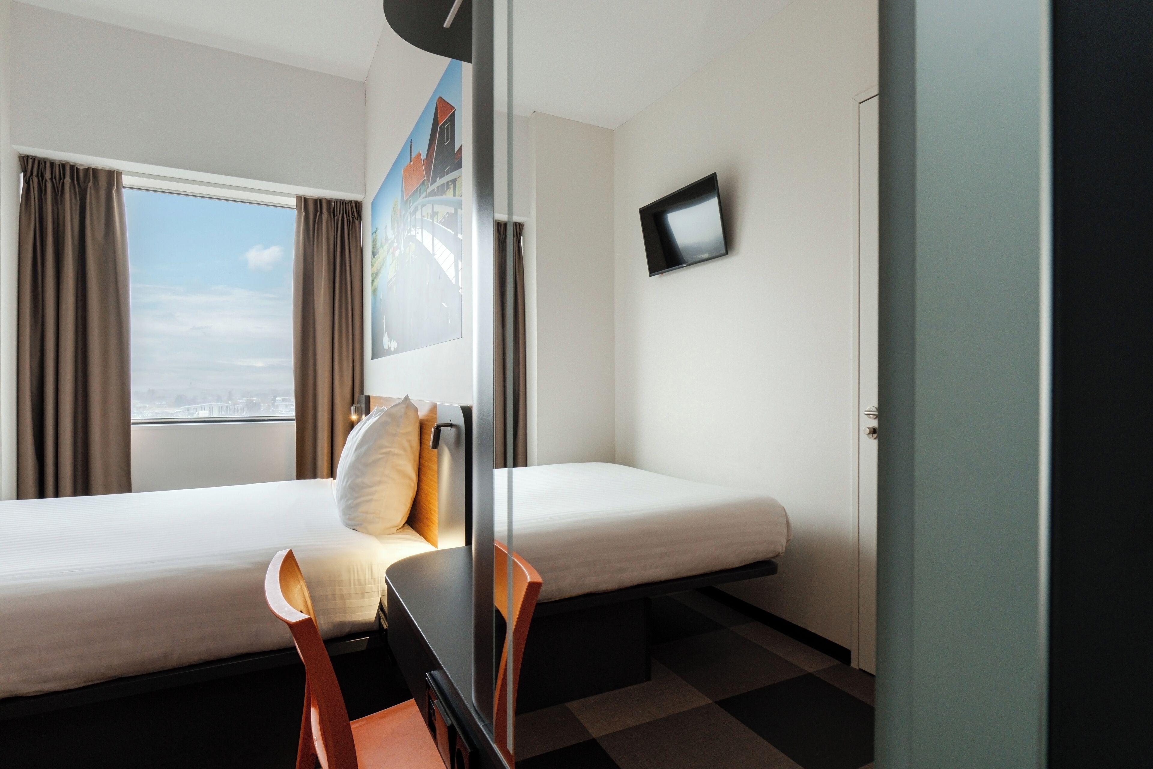 Ein Hotelzimmer mit zwei Betten, einem Schreibtisch, einem Sessel, einem Fernseher und einem Fenster mit Vorhängen.