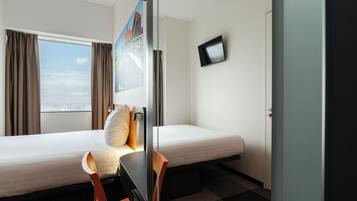 Ein Hotelzimmer mit zwei Betten, einem Schreibtisch, einem Sessel, einem Fernseher und einem Fenster mit Vorhängen.