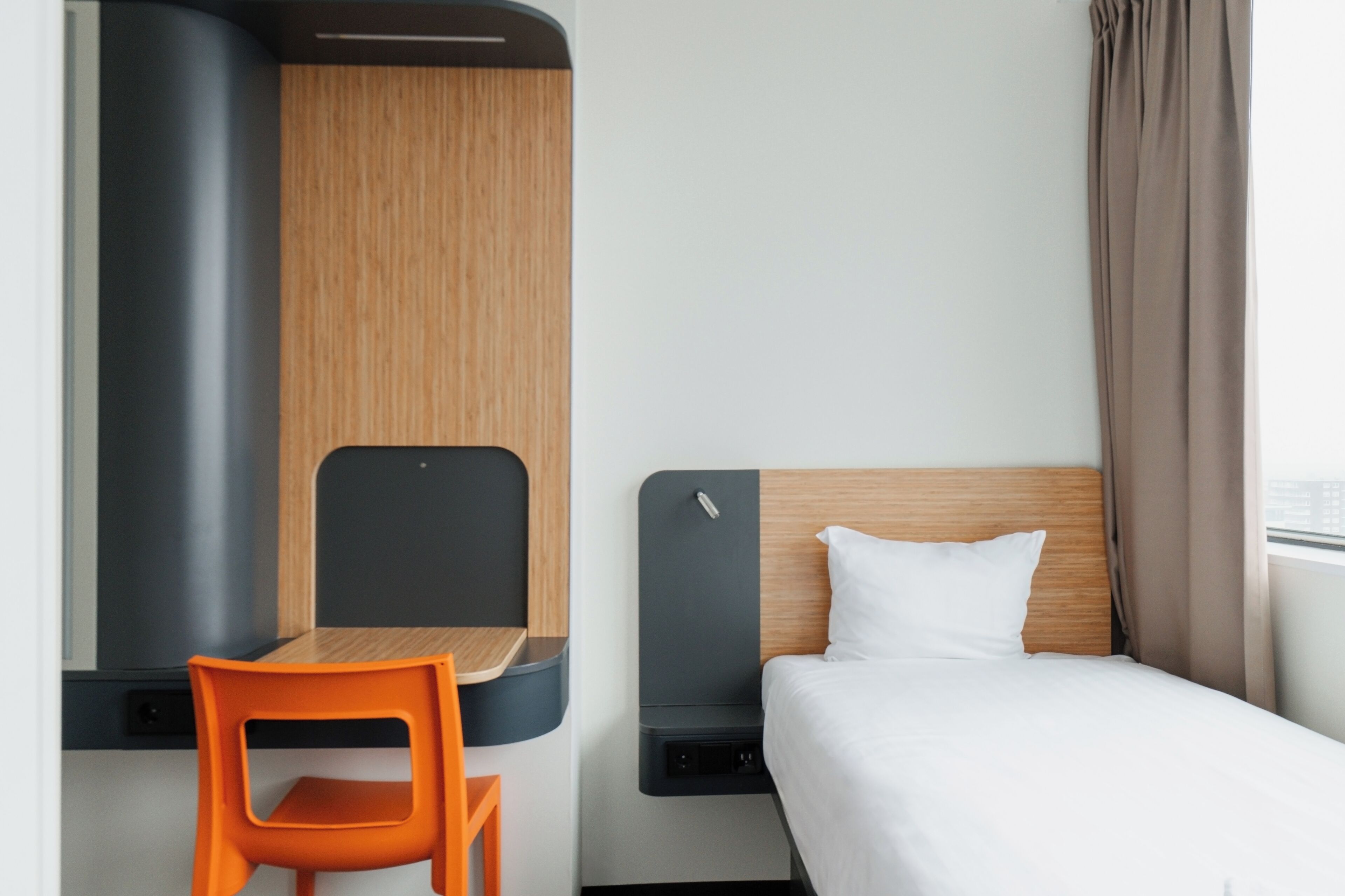 A modern hotel room with a bed, a desk, and a chair.