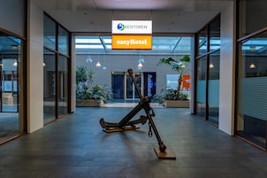 Un vestíbulo moderno con una gran escultura de ancla, paredes de vidrio y carteles que indican 'Saentorén' y 'easyHotel'.