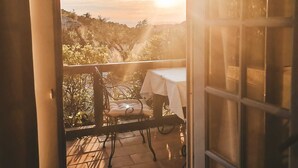 An open door leading to a balcony with a table and chairs, overlooking a hilly landscape during sunset. - Residence Le Mouron Rouge (La Garde-Freinet)