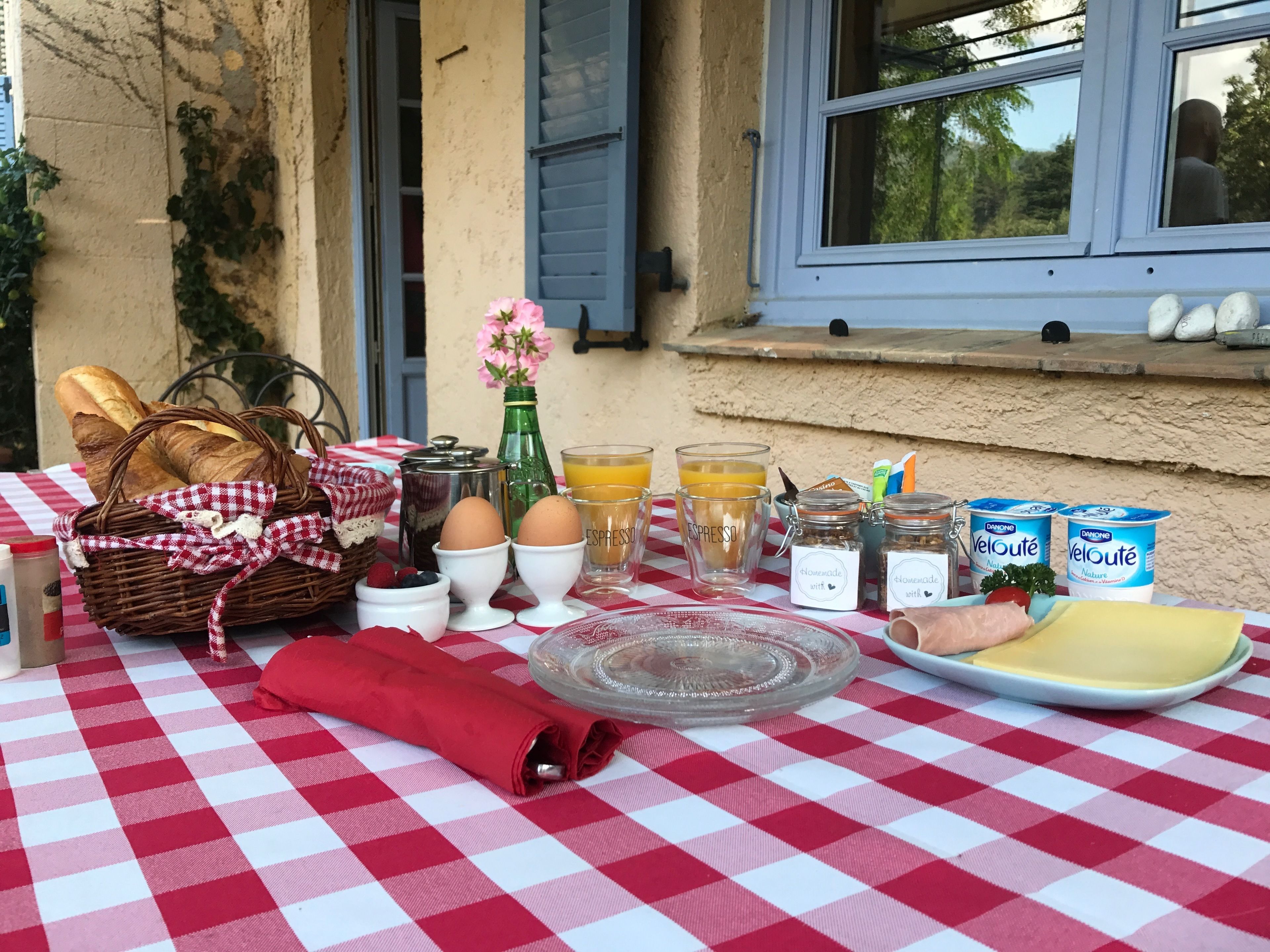Un desayuno con pan, huevos, jugo y productos lácteos sobre un mantel a cuadros.