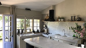 A kitchen with a large island, white tiled backsplash, and a window with curtains. - Residence Le Mouron Rouge (La Garde-Freinet)