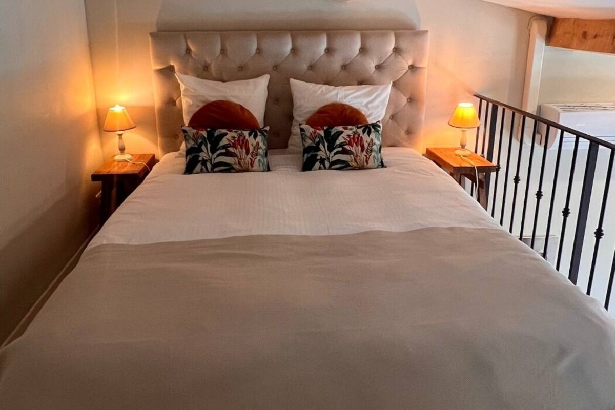 A bedroom with a tufted headboard, two bedside tables with lamps, and a balcony railing.