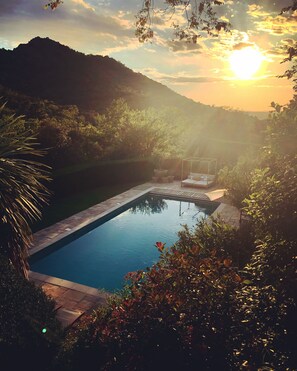Una piscina rectangular con borde transparente, rodeada de abundante vegetación y vistas a una cadena montañosa.