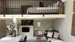 A cozy interior with a dining area, a sofa, a TV, and a staircase leading to a loft. - Residence Le Mouron Rouge (La Garde-Freinet)