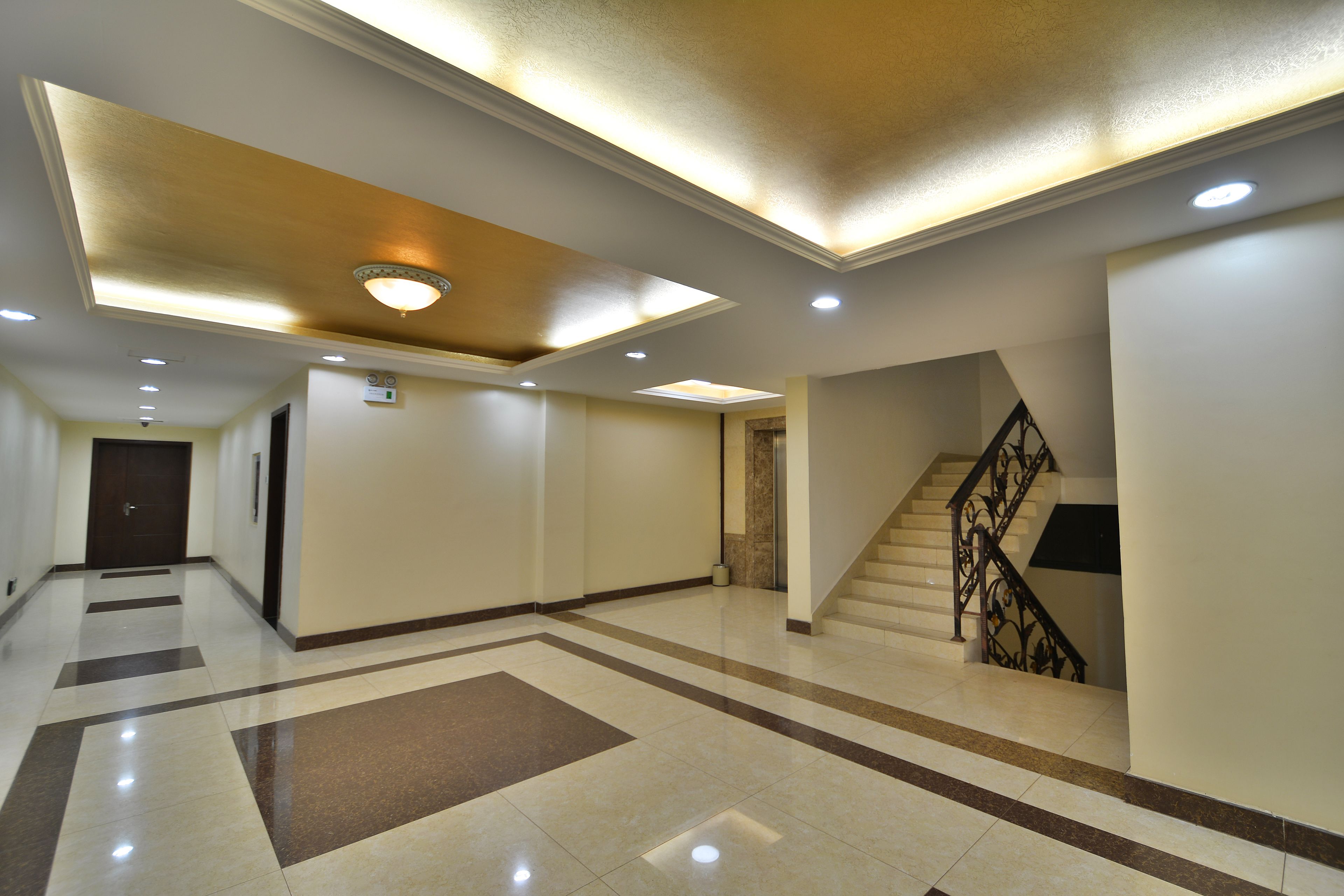 A spacious hallway with a staircase, recessed lighting, and a tiled floor.