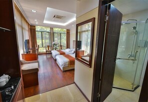 A hotel room with a large bed, a separate seating area, a TV, and a glass-enclosed shower. - Arirang Hotel (Kampala)