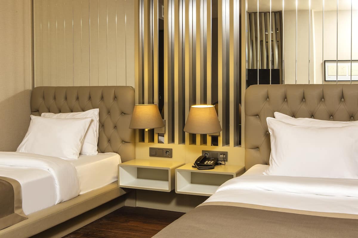 A hotel room with two beds, a bedside table with a lamp, a phone, and a mirror.