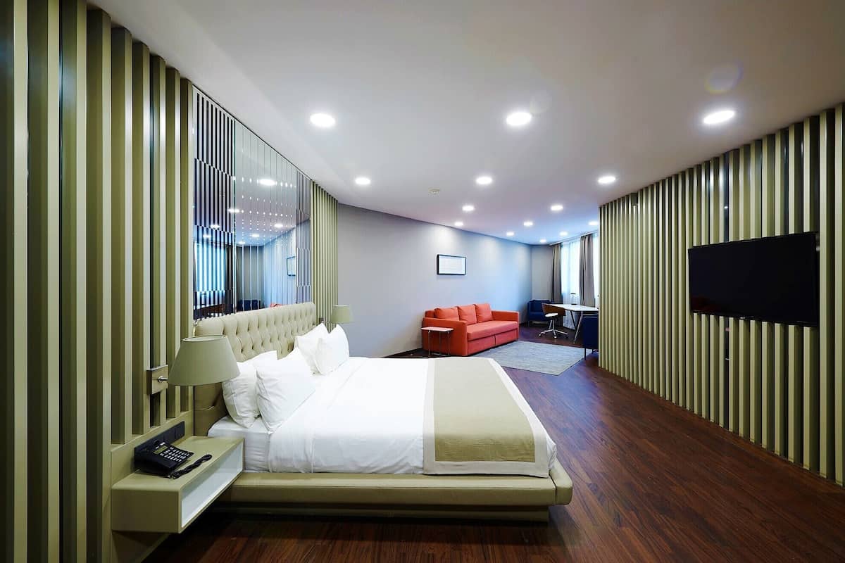 A modern hotel room with a large bed, a sofa, a TV, and a desk.
