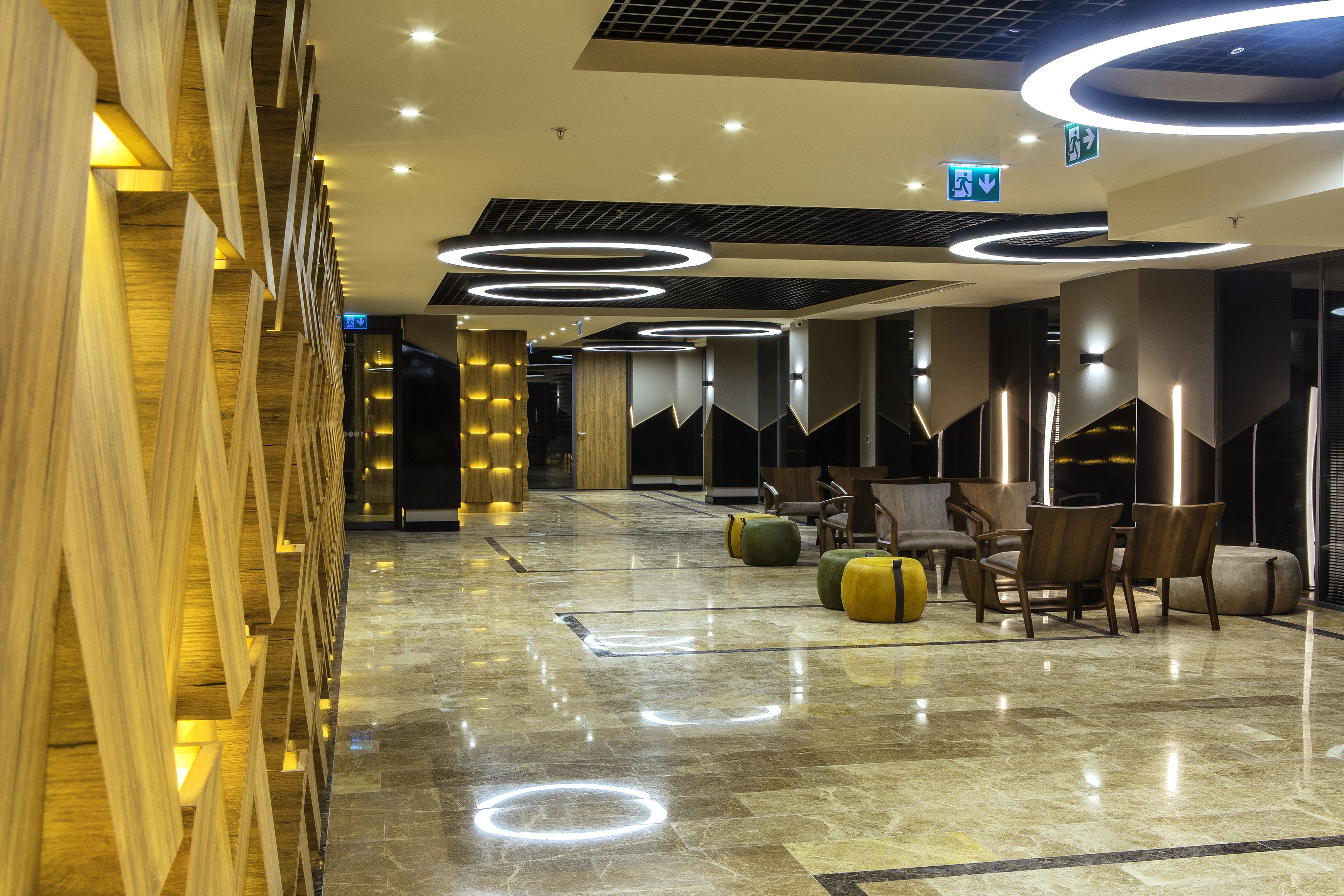 A modern lobby with a polished marble floor, wooden wall panels, and circular ceiling lights.