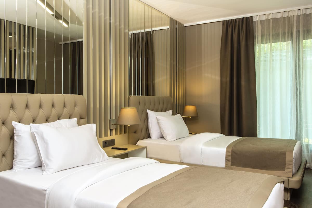 A hotel room with two beds, a large mirror, and a window with curtains.