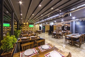 A restaurant with multiple dining tables and chairs, a modern ceiling design, and a green screen displaying a sports game. - Hann Hotel (Istanbul)