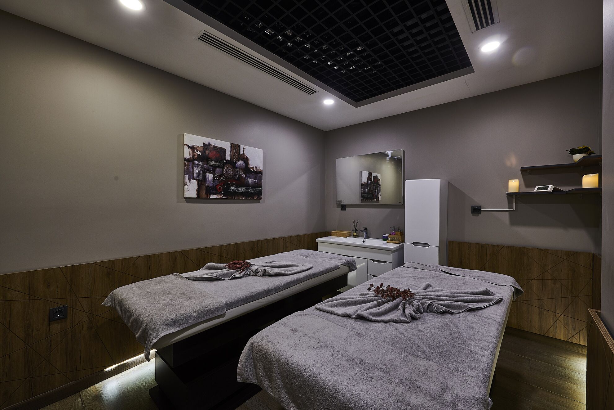 Un cuarto de spa con dos camillas de masaje, un espejo grande y una repisa con velas.