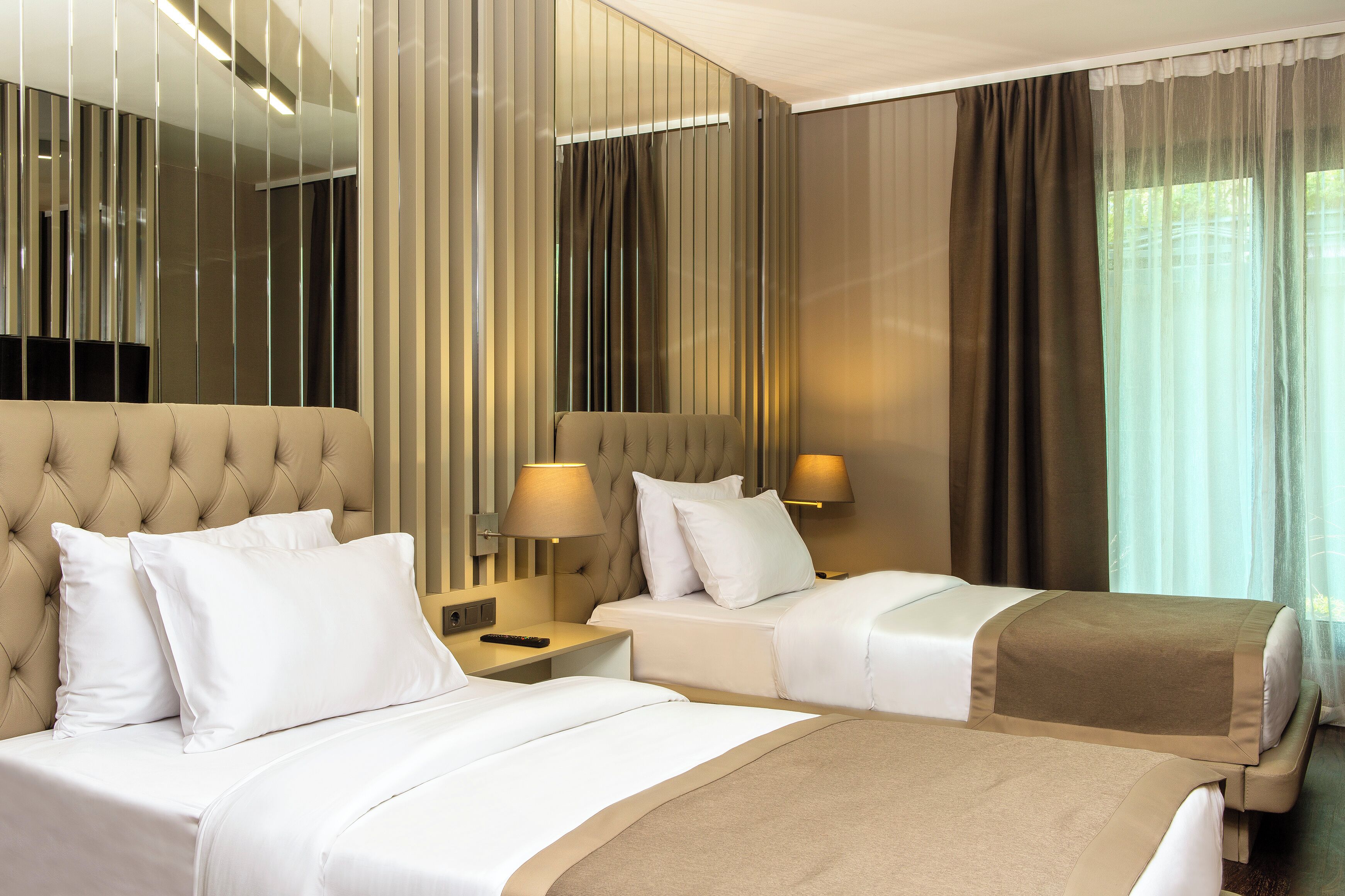 Habitación de hotel con dos camas, un espejo grande y vistas al exterior.