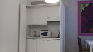 Cocina compacta con armarios blancos, microondas y una lámpara colgante.