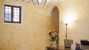 Una habitación con piso a cuadros, un escritorio de madera con una lámpara, una computadora portátil y un florero con flores.