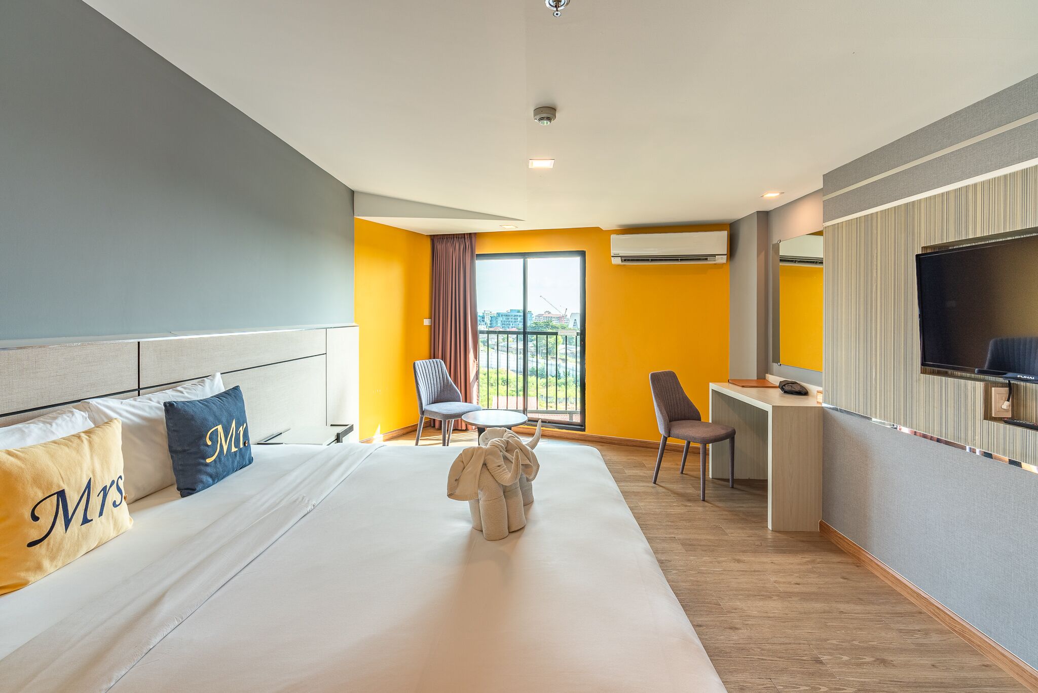 A hotel room with a large bed, two chairs, a desk, and a TV.