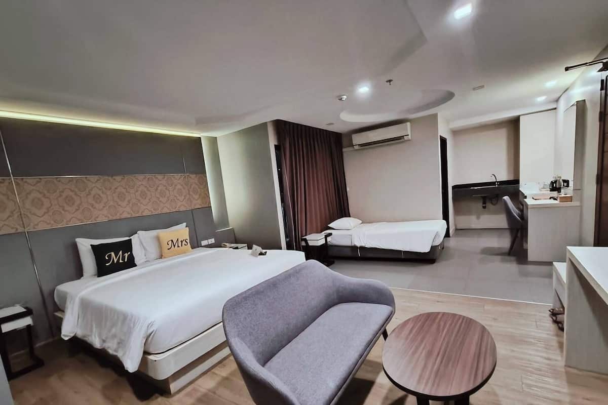 Ein modernes Hotelzimmer mit einem großen Bett, einer Couch, einem kleinen runden Tisch, einem Schreibtisch und einer Klimaanlage.