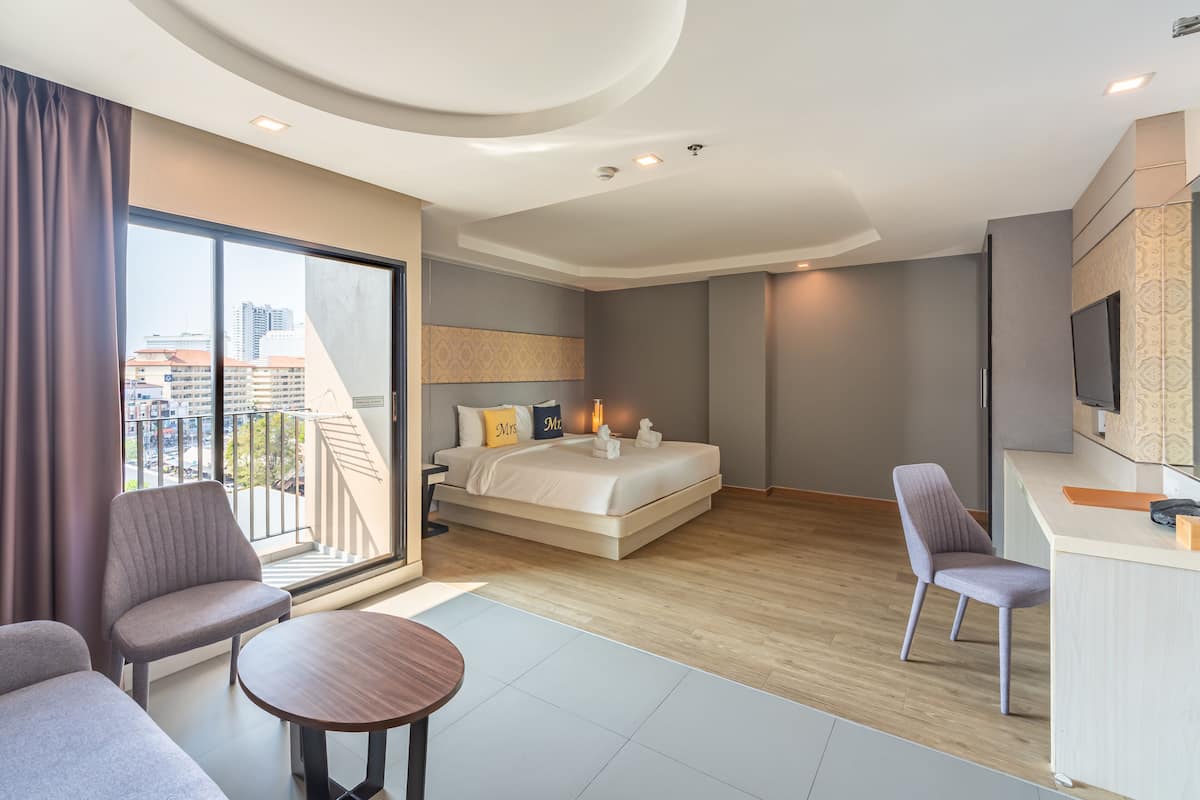 Ein modernes Hotelzimmer mit einem großen Bett, einem Schreibtisch, einem Sessel und einem Balkon mit Blick auf die Stadt.