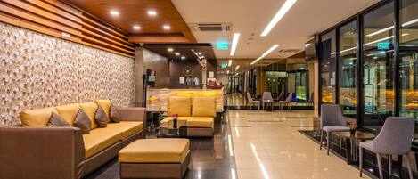 A modern lobby with a sofa, ottoman, and chairs, a patterned wall, and a glass wall with a view.