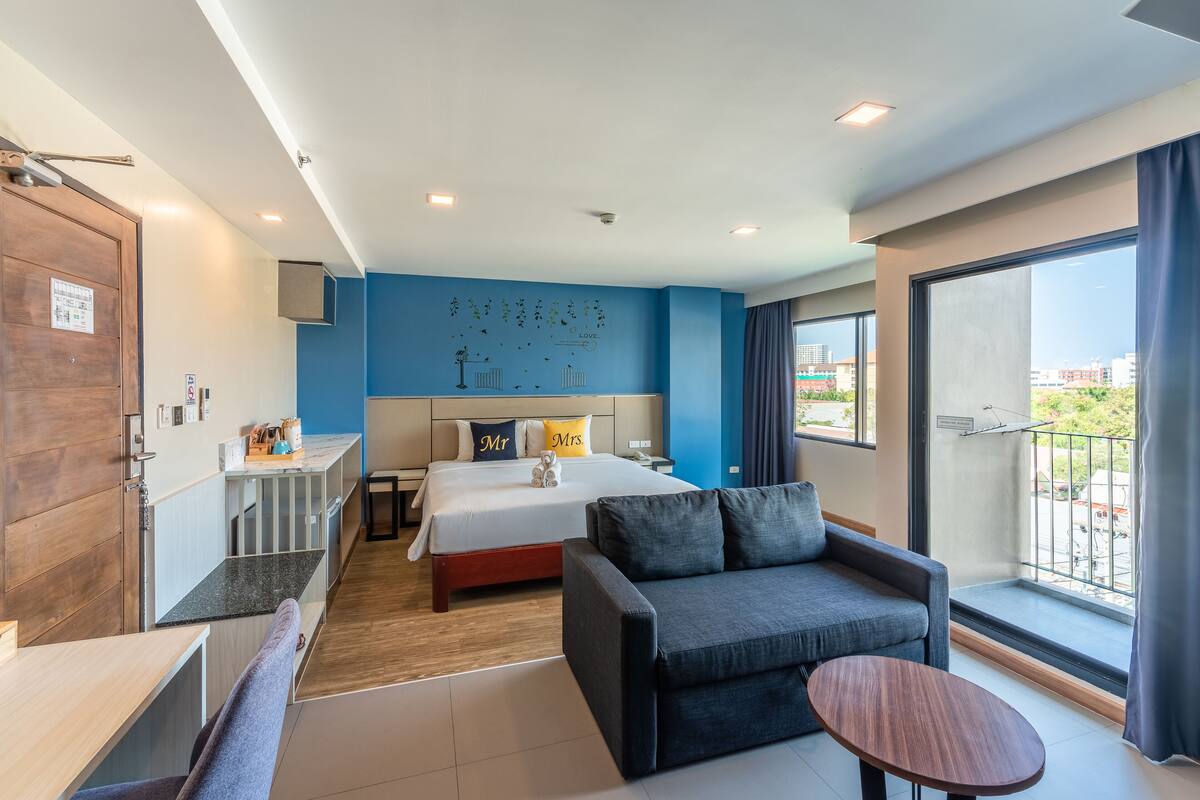 Ein modernes Hotelzimmer mit einem großen Bett, einer Couch, einem kleinen Tisch und einem Balkon mit Blick auf die Stadt.