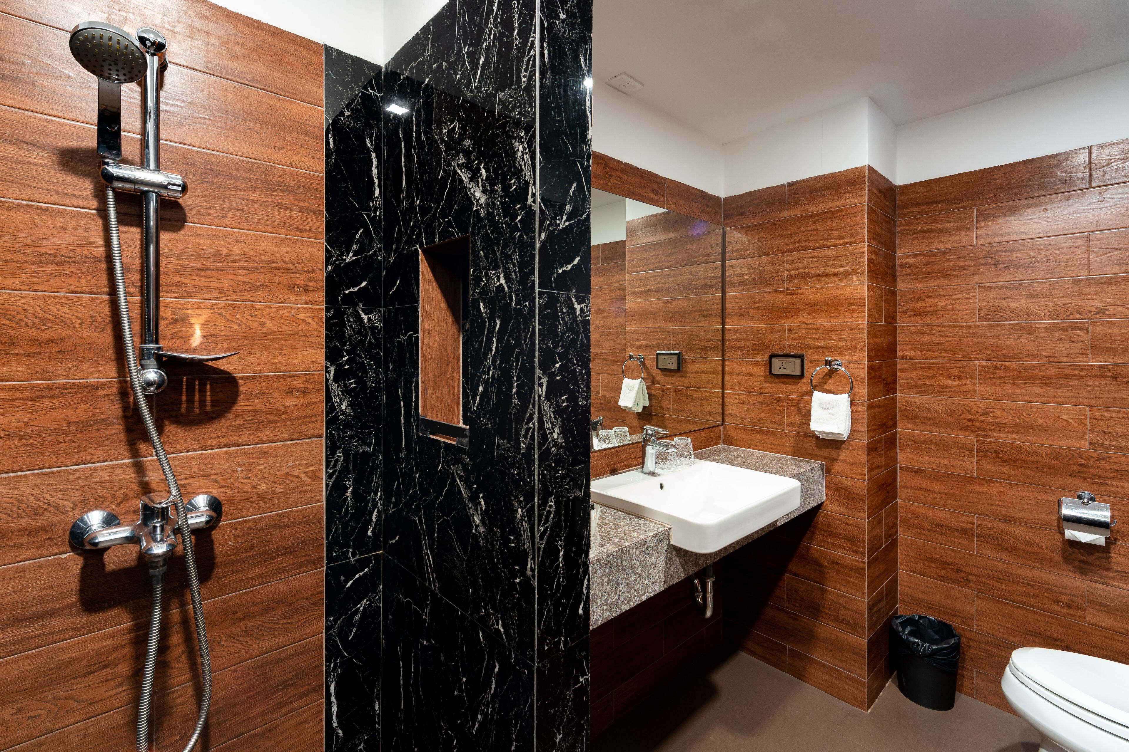 Un baño moderno con tocador de madera, cabina de ducha de mármol negro y un inodoro blanco.