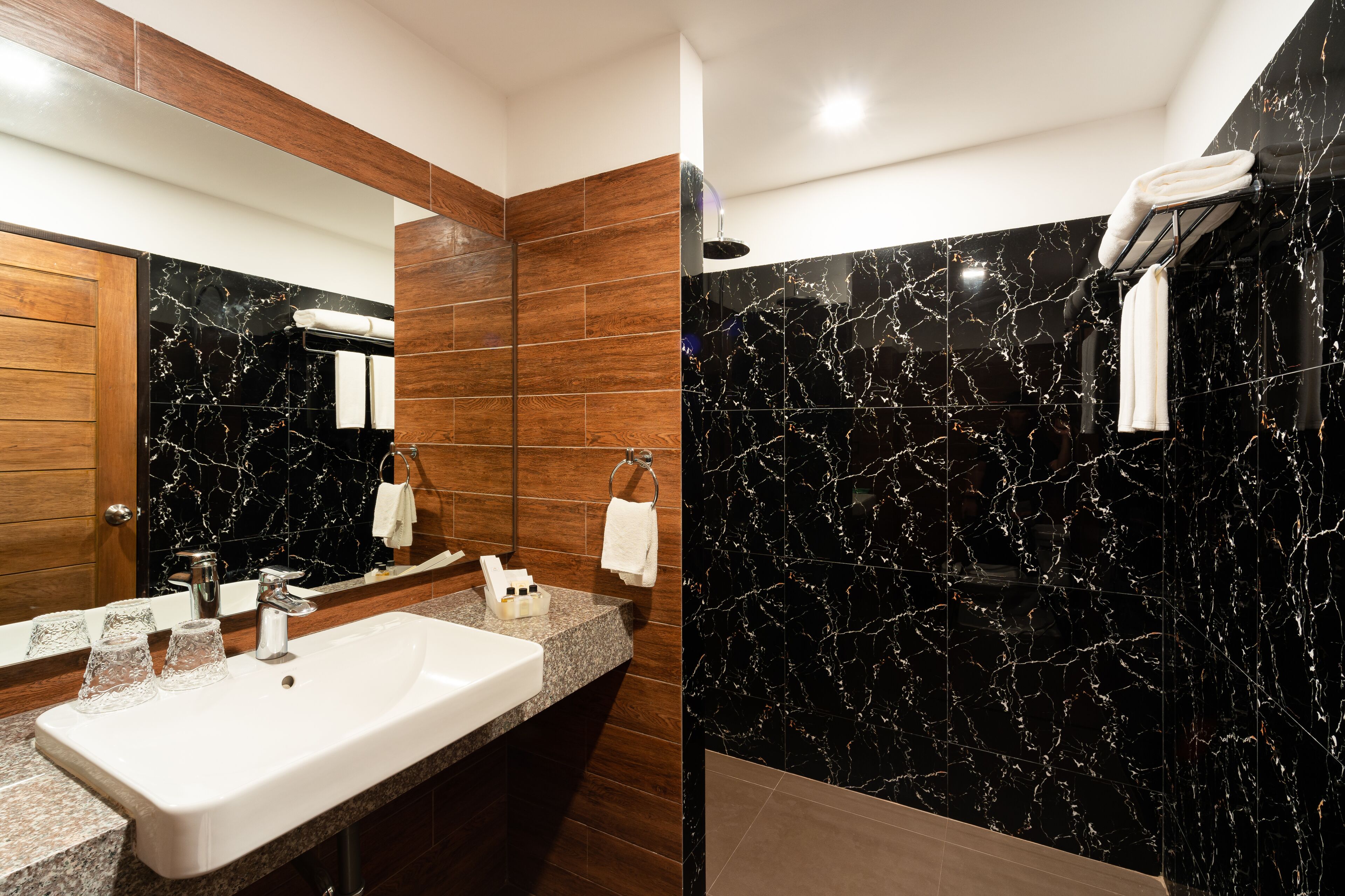 A modern bathroom with a marble sink, wooden vanity, and a shower area.