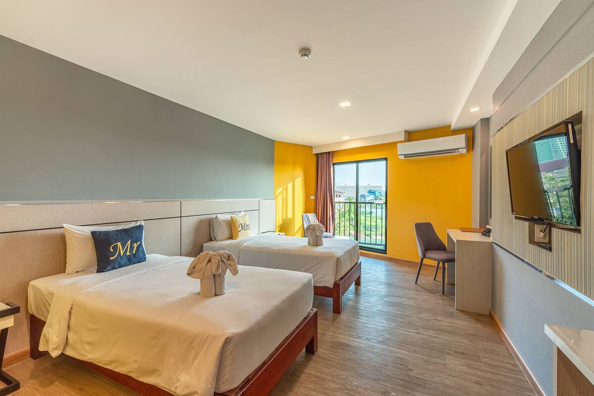 Ein Hotelzimmer mit zwei Betten, einem Schreibtisch, einem Fernseher und einem Balkon mit Blick.