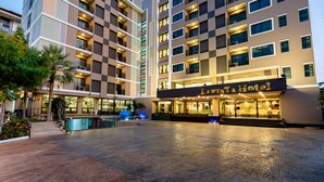 Un hôtel à plusieurs étages au design moderne, doté d’une entrée imposante avec une enseigne, d’une cour avec des sièges et d’un espace piscine.