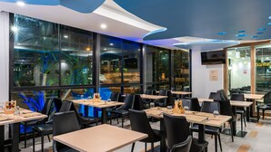 Un restaurant doté de nombreuses tables et chaises, de grandes fenêtres et d’un plafond au design moderne.