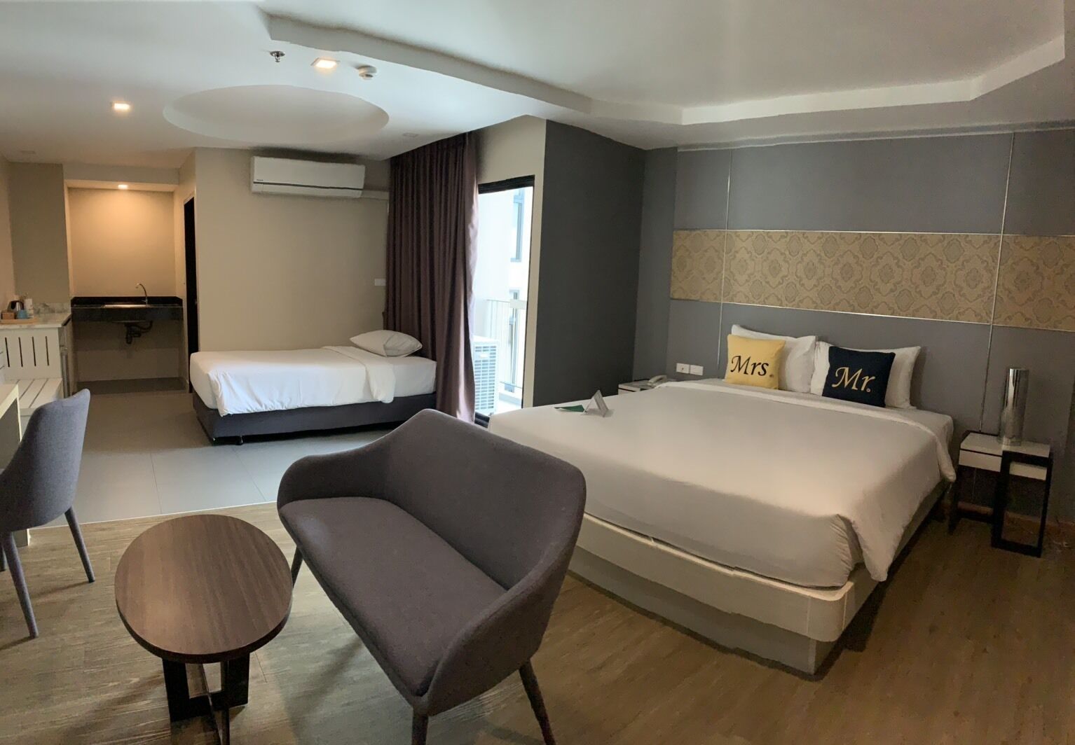 A hotel room with a large bed, a smaller bed, a sofa, a desk, and a chair.