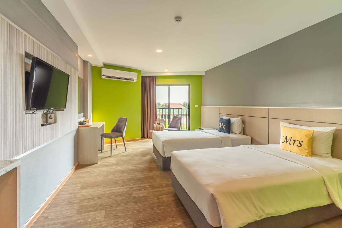 Ein Hotelzimmer mit zwei Betten, einem Schreibtisch, einem Sessel, einem Fernseher und einer Klimaanlage.
