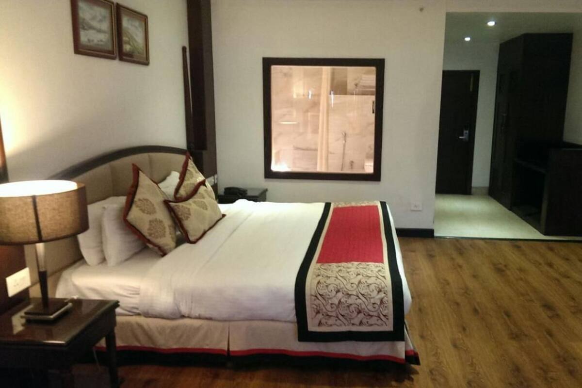 A hotel room with a bed, a nightstand, a lamp, a framed picture on the wall, and a view of a bathroom.