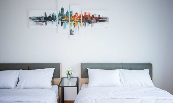 Two single beds with grey headboards and white bedding, complemented by a bedside table and framed cityscape artworks.