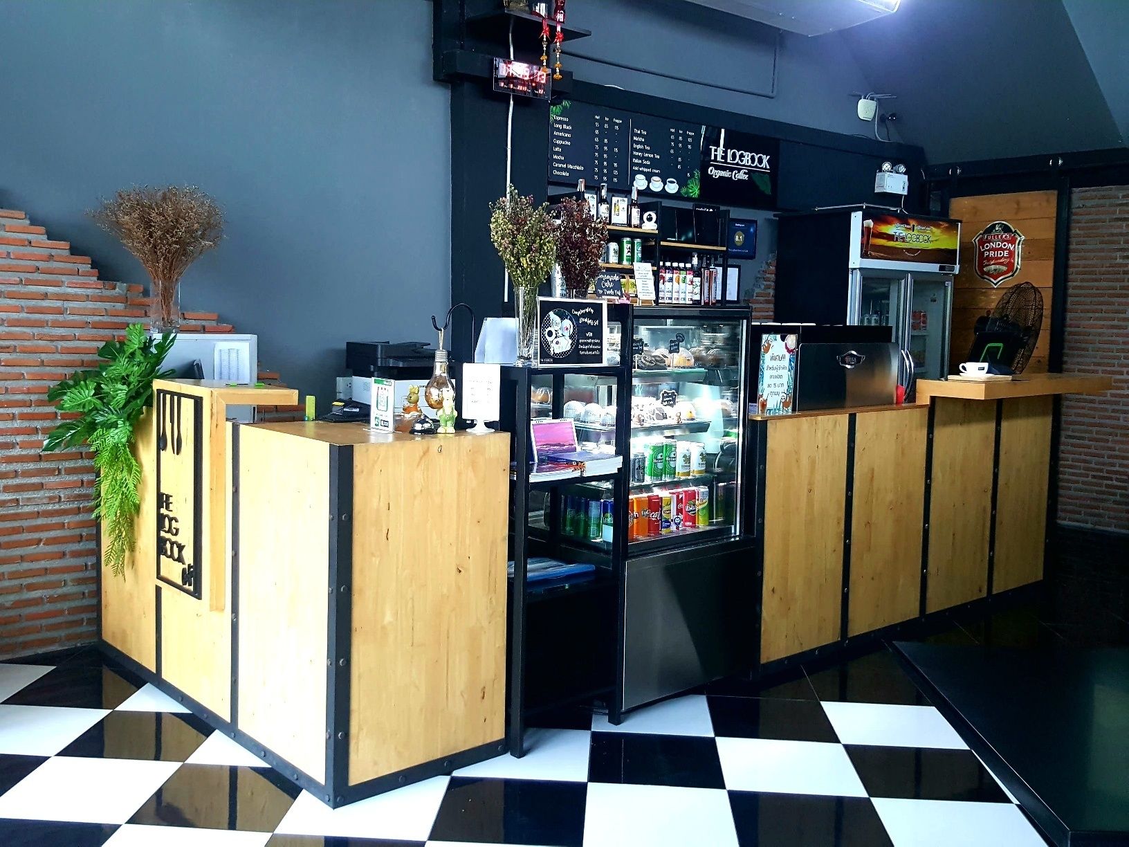 Ein Tresen in einem Café mit einer Speisekarte, einem mit Getränken gefüllten Kühlschrank und einer Backsteinwand im Hintergrund.