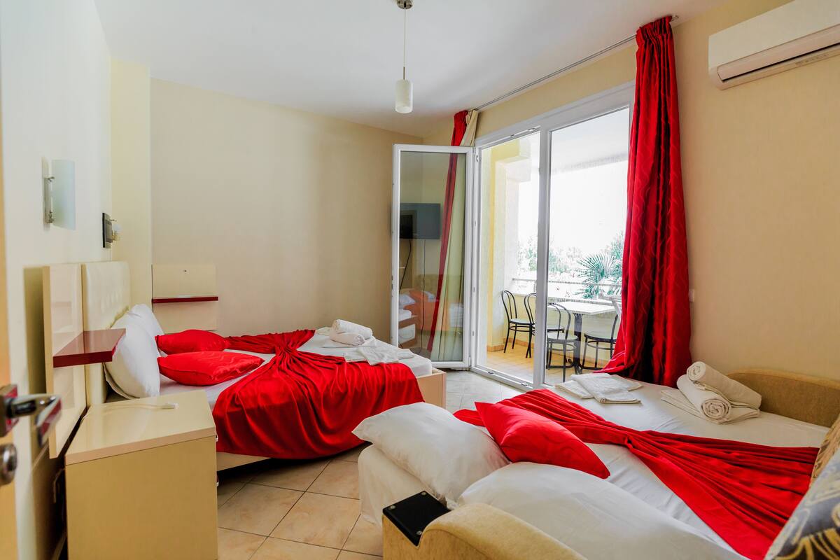 A hotel room with two beds, a sliding glass door to a balcony, a small table, and a chair.