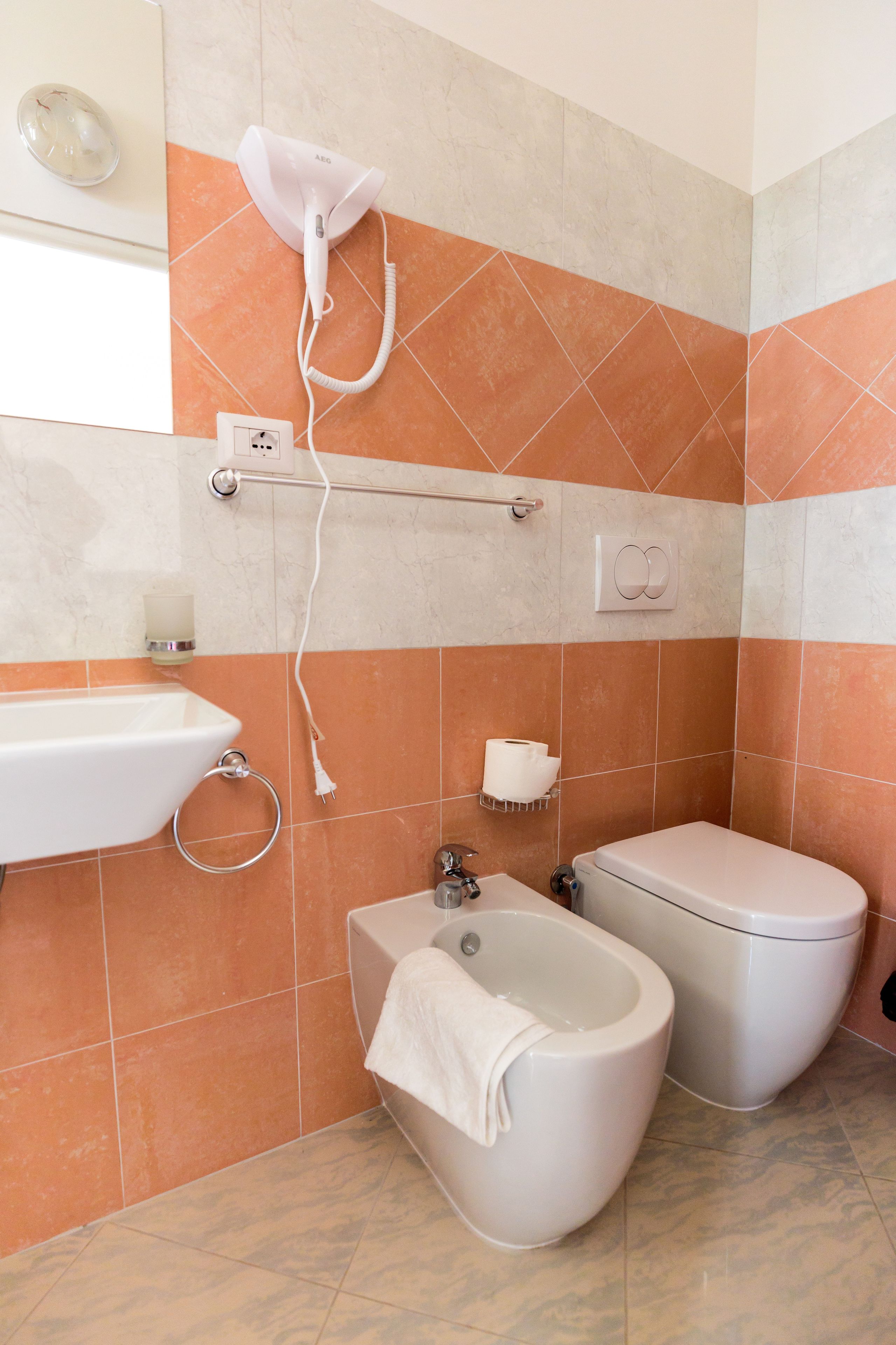 A bathroom with a bidet, toilet, sink, and a towel rack.