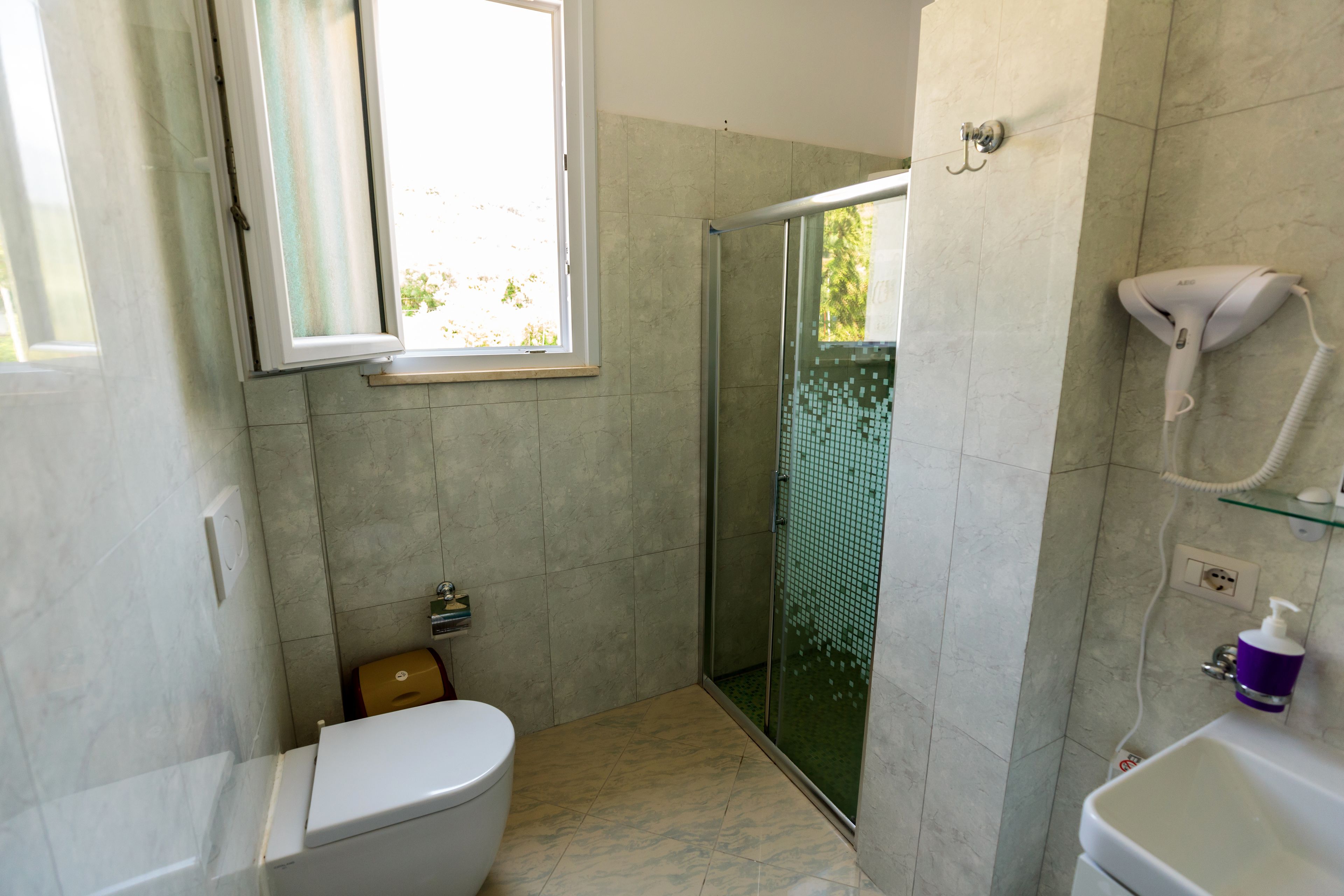 Un baño con inodoro, ducha con puerta de vidrio y secador de pelo en la pared.