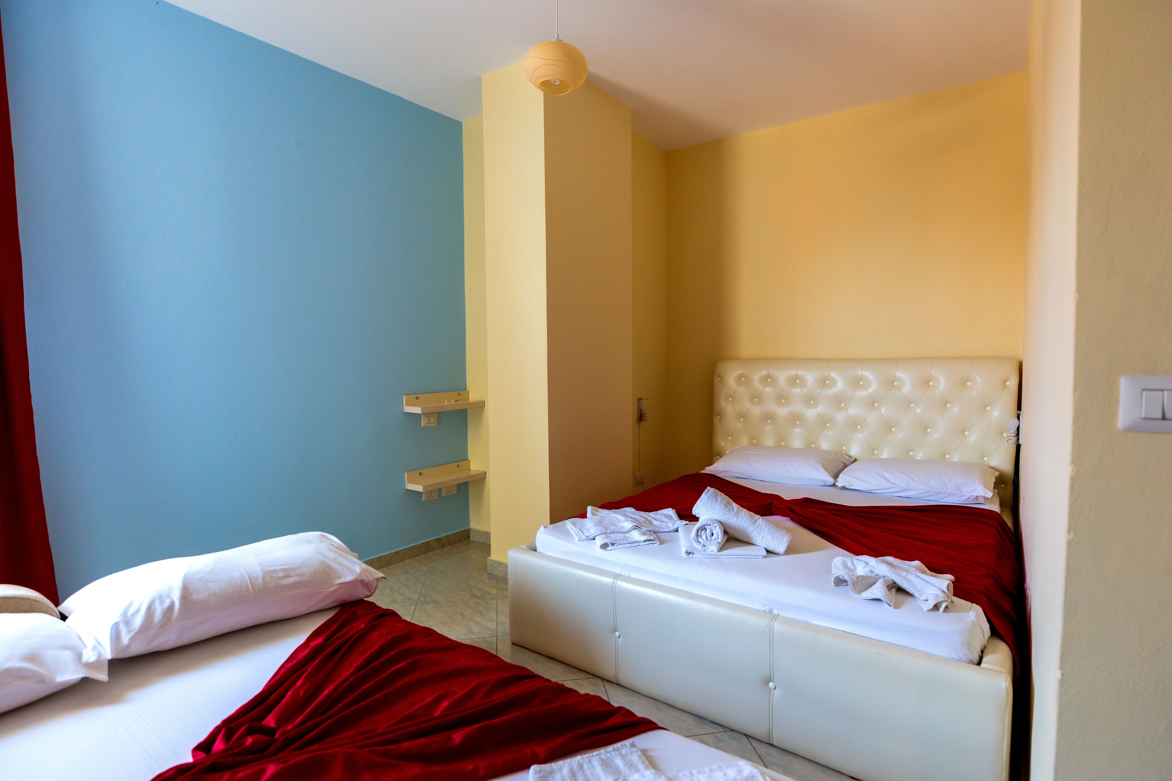 Habitación de hotel con dos camas, una colcha roja y blanca, cabecera blanca y una lámpara colgante.