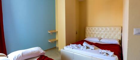 Habitación de hotel con dos camas, una colcha roja y blanca, cabecera blanca y una lámpara colgante.
