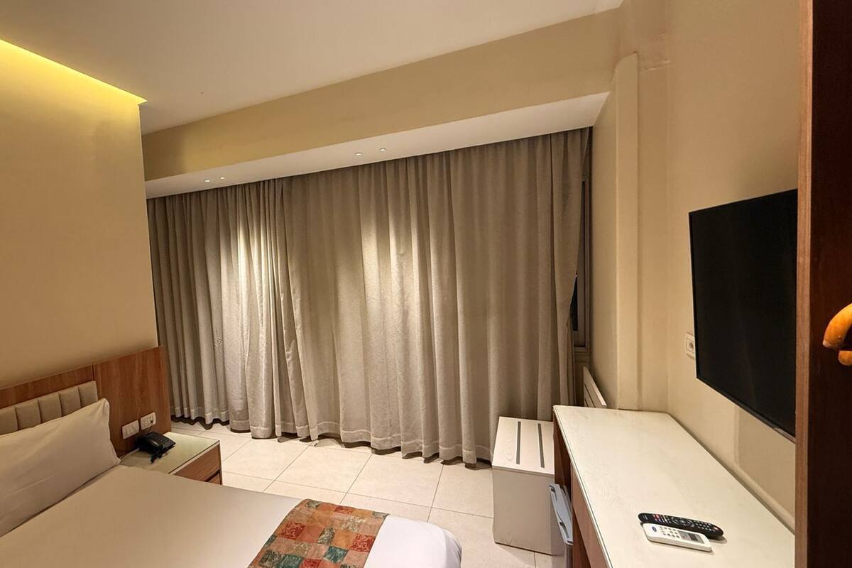 A hotel room with a bed, bedside table, lamp, curtains, and a TV.