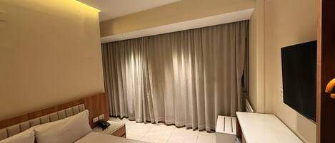 A hotel room with a bed, bedside table, lamp, curtains, and a TV.