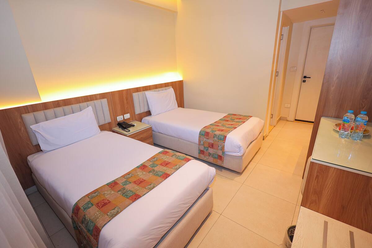 A hotel room with two beds, a small desk, and a door.