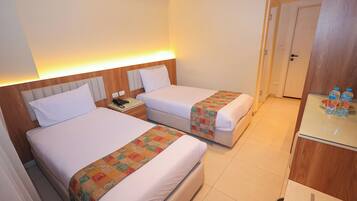 A hotel room with two beds, a small desk, and a door.