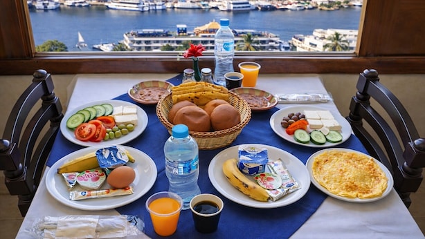A breakfast table with various food items, a bottle of water, and a view of a marina. - Hapi Hotel (Aswan)