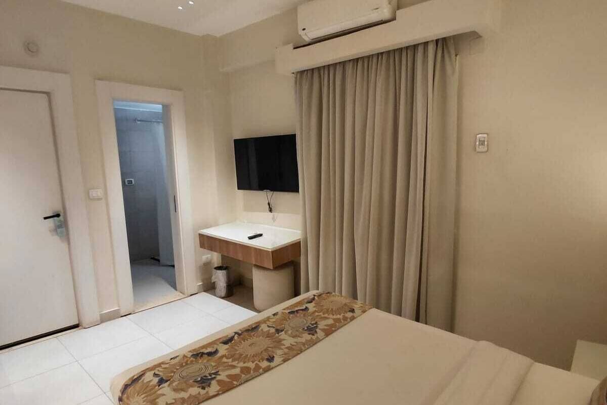 A hotel room with a bed, a desk, a television, and an air conditioning unit.