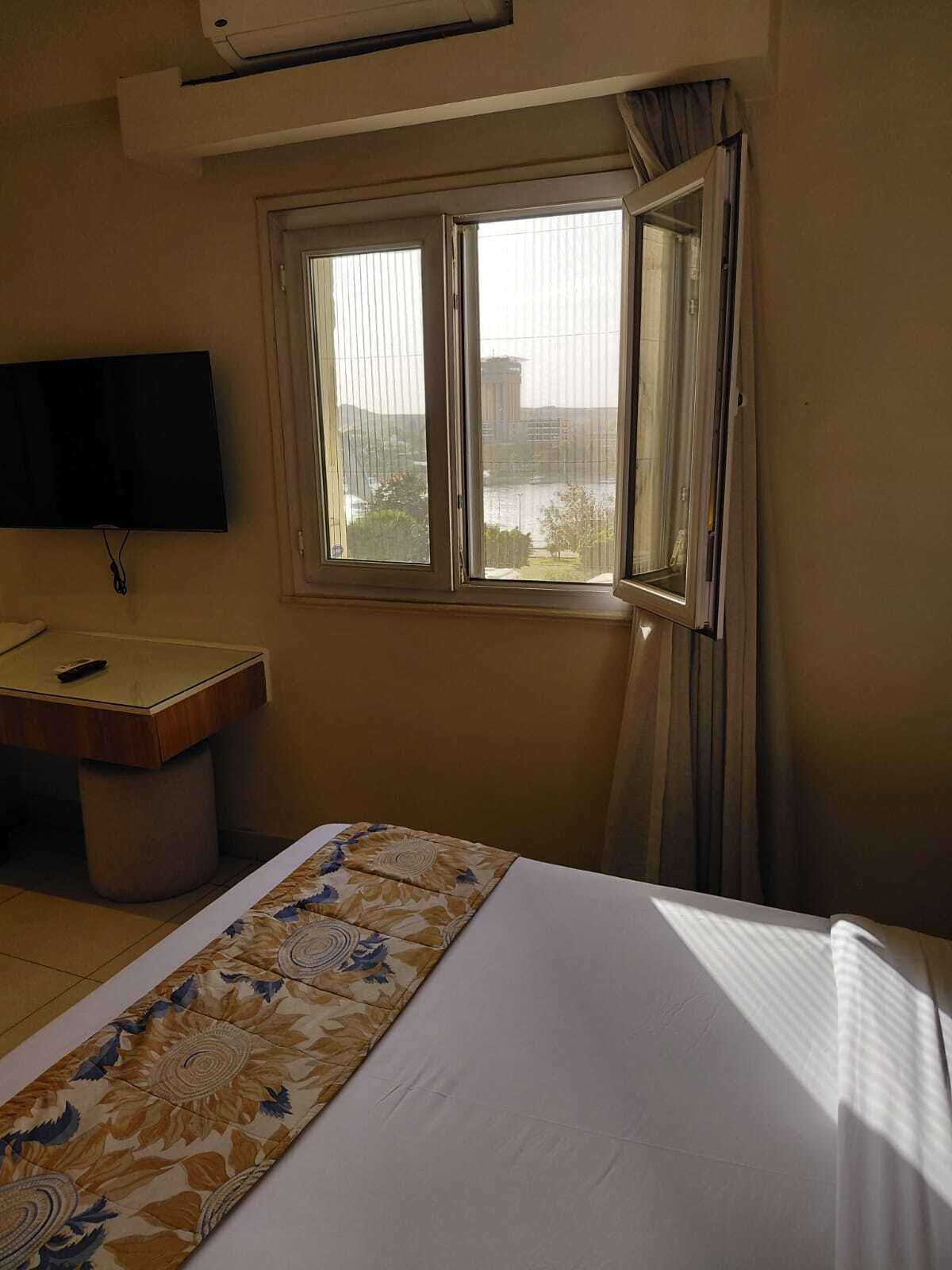 A hotel room with a bed, a desk, a television, and a window with a view of a building and a body of water.