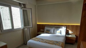 A hotel room with a bed, bedside tables, a mirror, a window, and a wall-mounted air conditioner. - Hapi Hotel (Aswan)