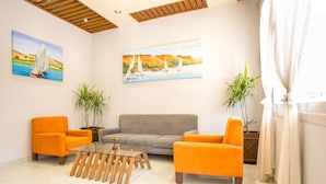 A modern living room with a glass coffee table, two orange armchairs, a grey sofa, and two potted plants. - Hapi Hotel (Aswan)